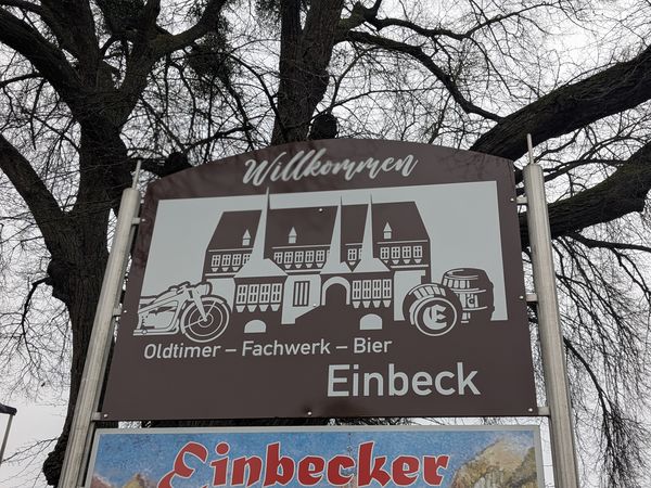 Straßenschild auf dem das Altes Rathaus Einbecks, eine altes Motorrad , hölzerne Bierfässer sowie die Worte Oldtimer, Fachwerk, Bier.
