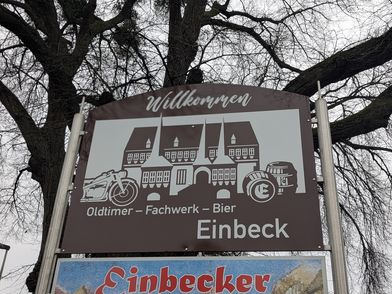 Straßenschild auf dem das Altes Rathaus Einbecks, eine altes Motorrad , hölzerne Bierfässer sowie die Worte Oldtimer, Fachwerk, Bier.