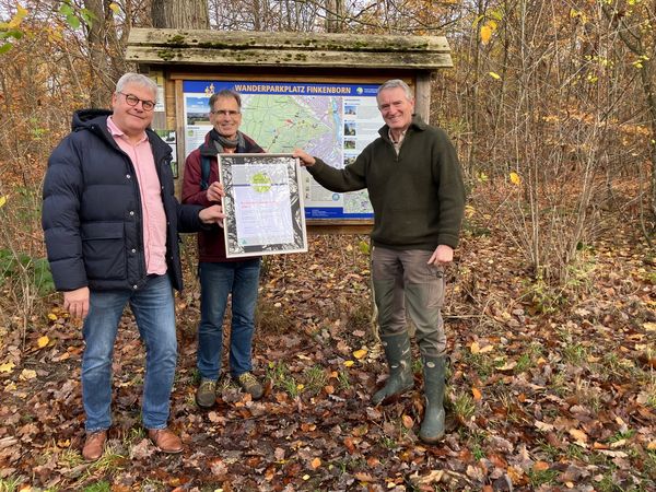 Frank Lücke von Hameln Marketing und Tourismus, Hans-Georg Sievers vom Naturpark Weserbergland und Carsten Bölts vom Hamelner Forstamt stehen mit der Urkunde im Wald