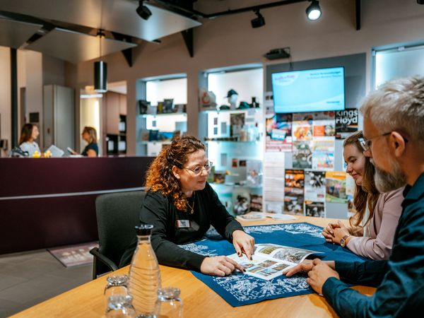 Mitarbeiterin berät zwei Gäste an einem Tisch in der Tourist-Information Einbeck.