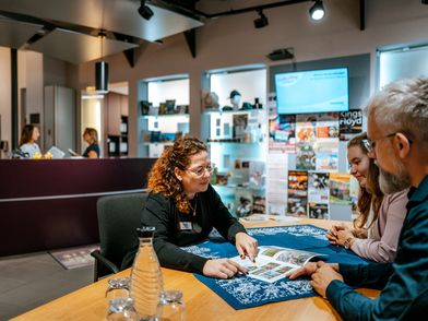 Tourist-Information Mitarbeiterin berät zwei Gäste an einem Tisch in der Tourist-Information Einbeck.