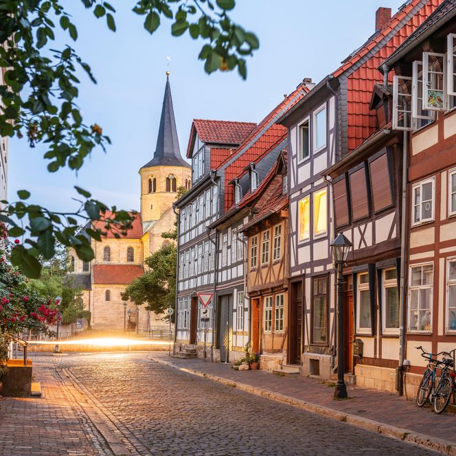 Seitlicher Blick auf eine Gasse mit Fachwerkhäusern im Fachwerkviertel in Hildesheim mit der Basilika St. Godehard im Hintergrund bei Abenddämmerung