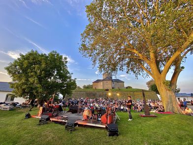 Veranstaltung Wilhelmstein Open-Air-Konzert auf einer grünen Wiese vor einer historischen Festung bei Sonnenuntergang.
