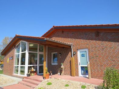 Eingang der Krippe Behringen mit rotem Backsteingebäude, Glasfenstern und Treppenstufen unter blauem Himmel