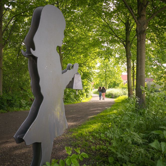 Skulptur von einem Mädchen am Wegrand von den Wallanlagen zwischen Bäumen und Sträuchern 
