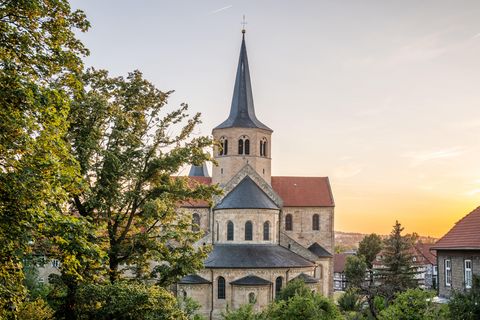 Sicht auf die Basilika St. Godehard vom Kehrwiederwall aus durch Bäume mit Sonnenuntergang im Hintergrund