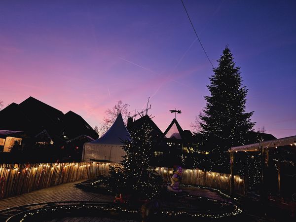 Blick auf das beleuchtete Weihnachtsdorf Rastede, mit violett gefärbtem Abendhimmel im Hintergrund