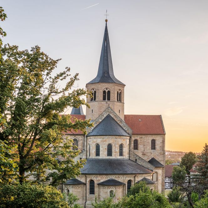 Sicht auf die Basilika St. Godehard vom Kehrwiederwall aus durch Bäume mit Sonnenuntergang im Hintergrund